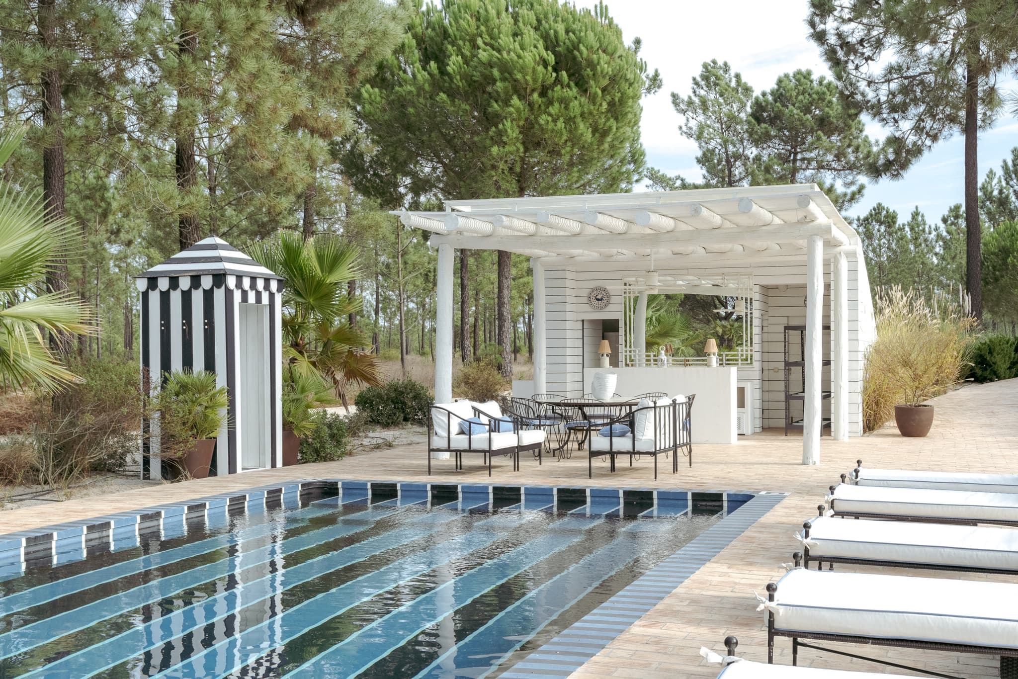 A swimming pool with a striped cabana under a pergola beside it