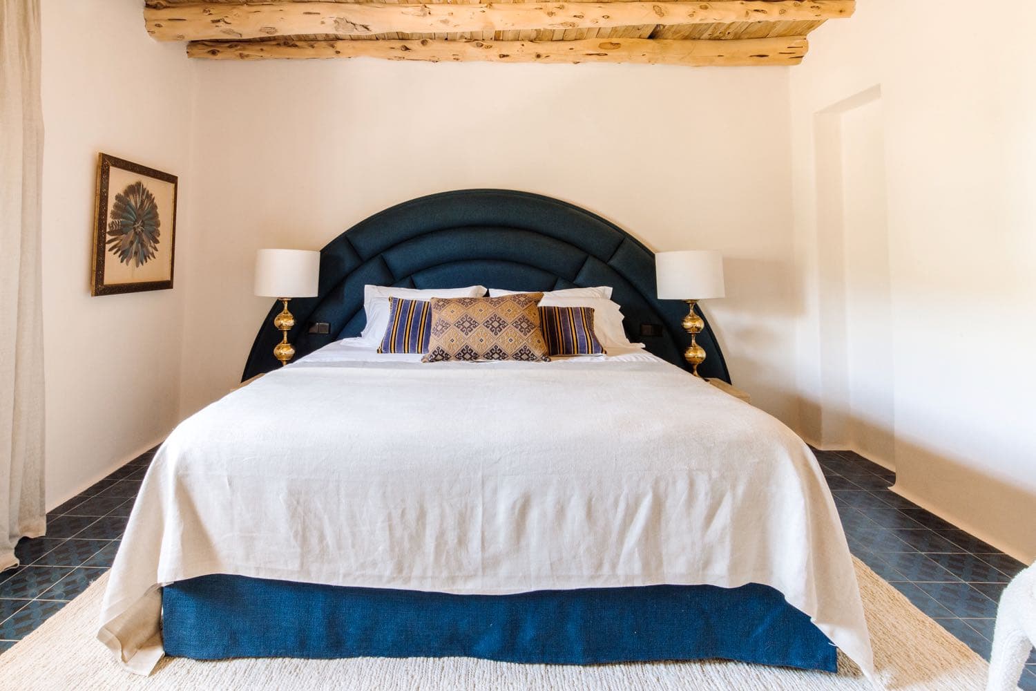 A navy arched headboard between brass lamps
