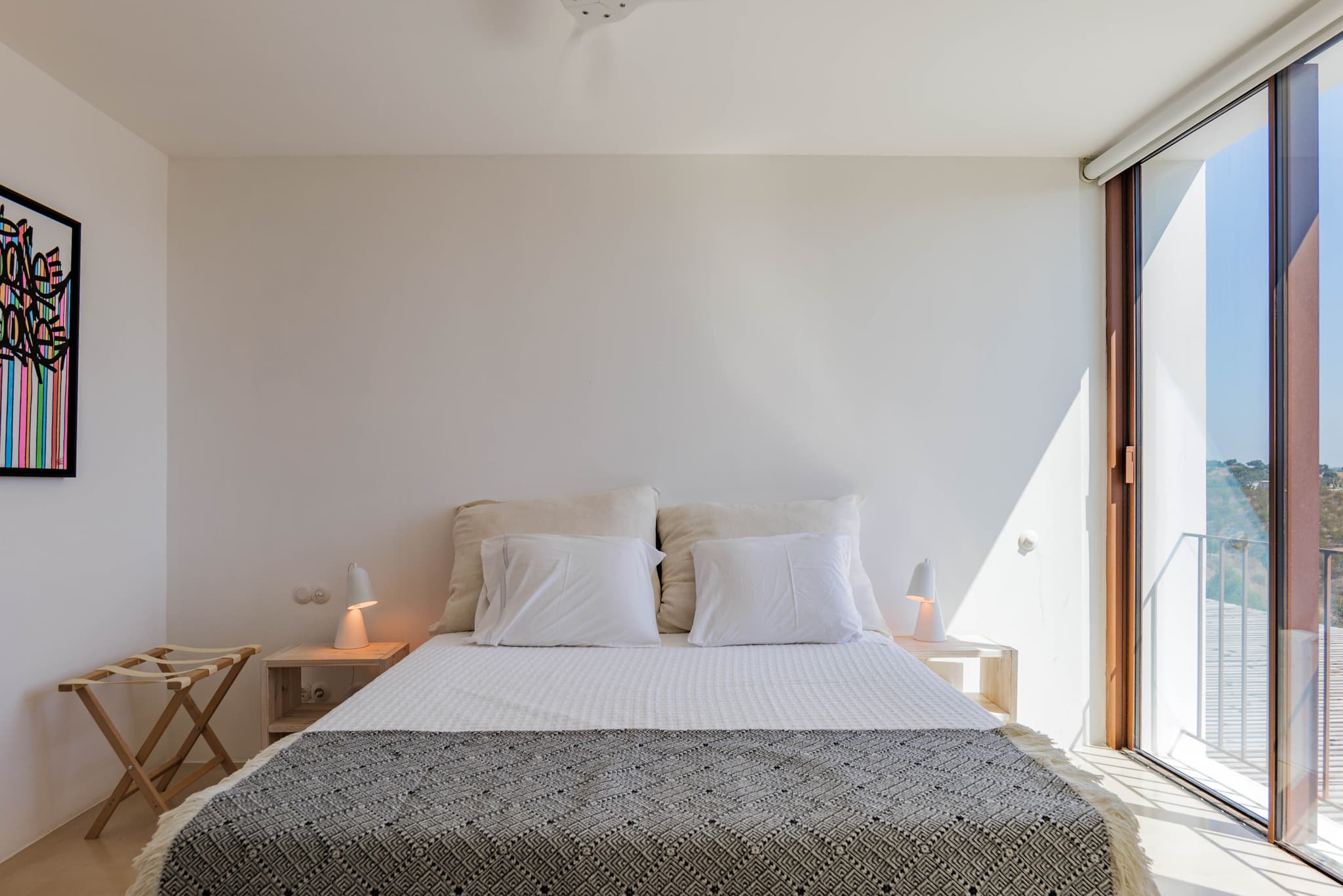 A bedroom under its floor to ceiling window, artwork on the wall